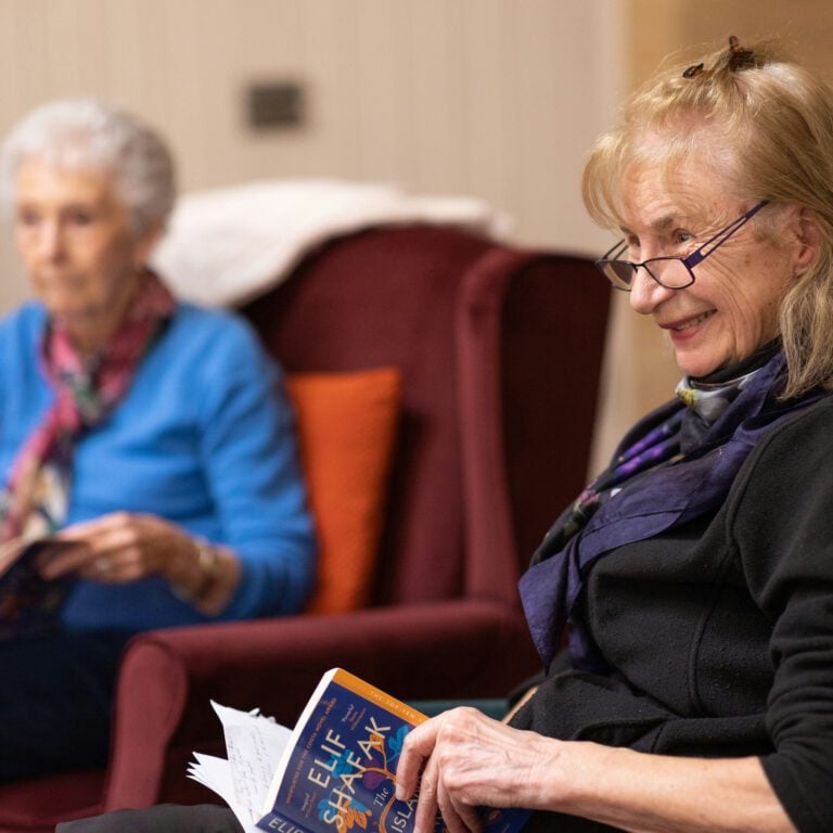 An elderly woman in a care home setting smiling at somebody off-camera