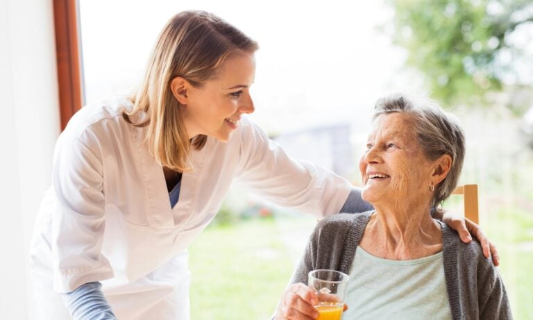 A nurse with her arm around an elderly woman drinking orange juice