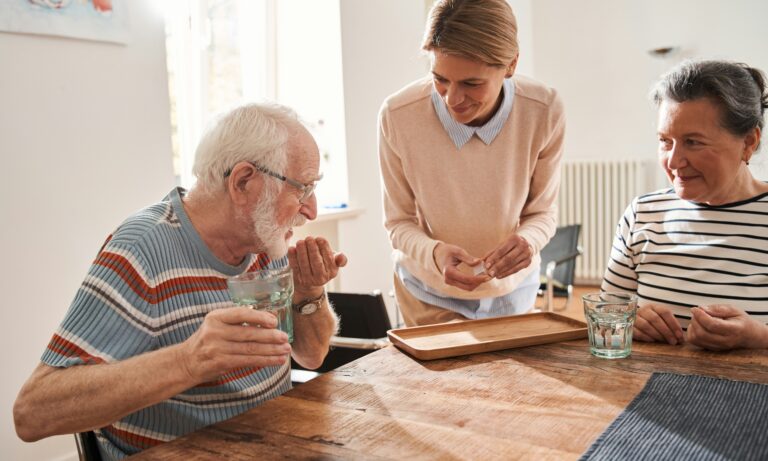 A home care assistant giving tablets to an elderly couple
