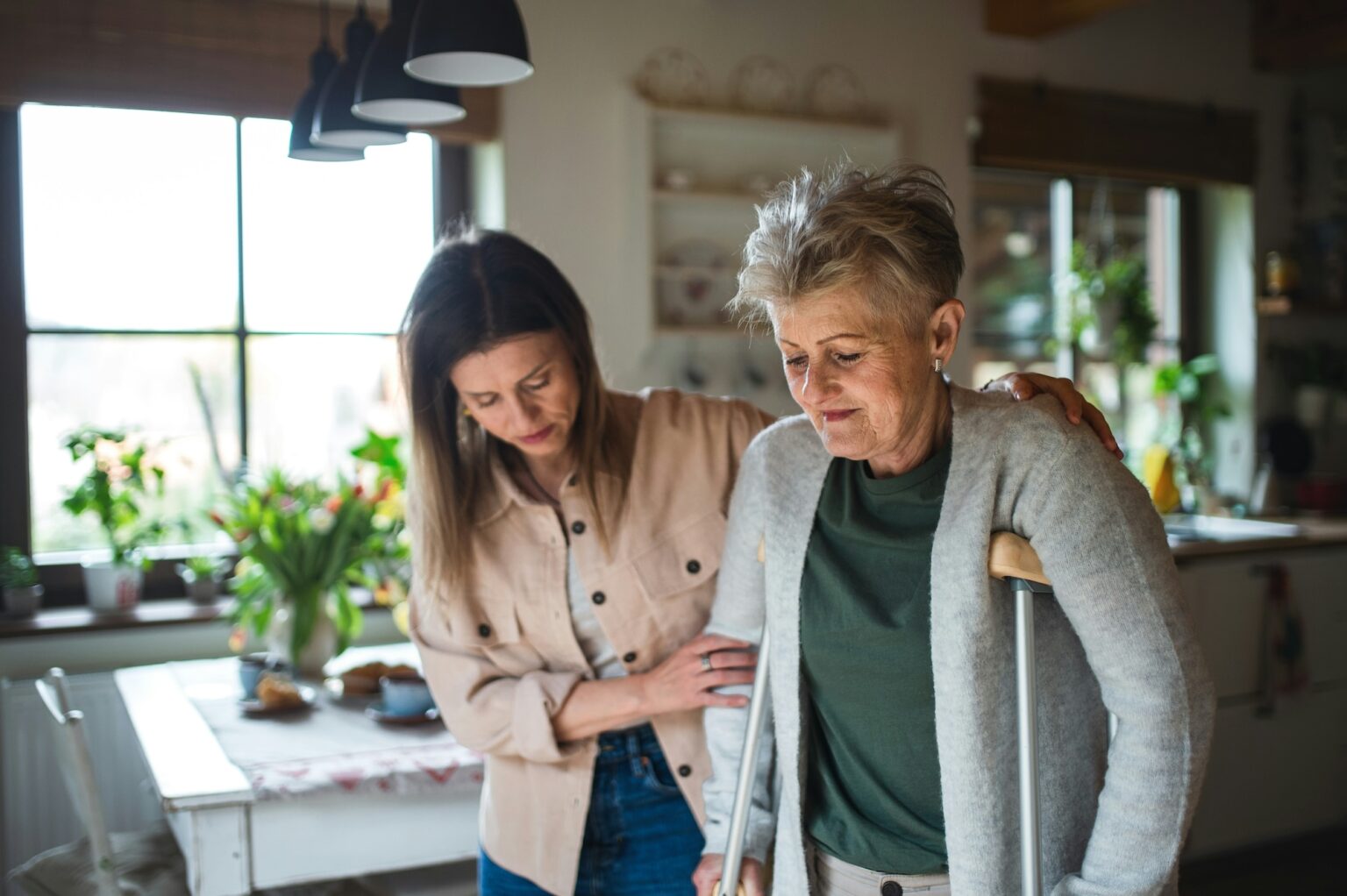 An adult woman helps an olderly woman on crutches