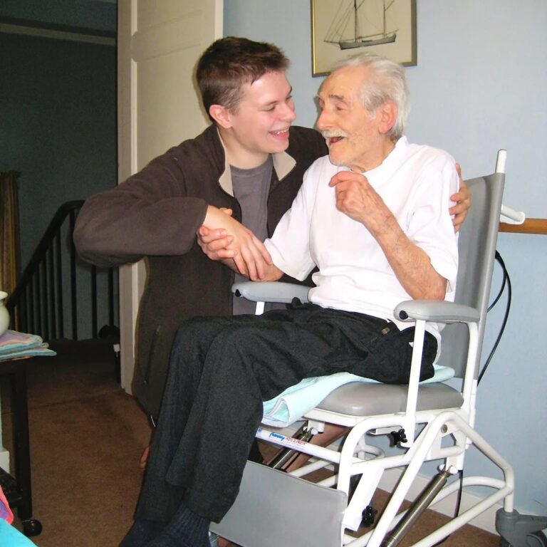 An elderly man in a wheelchair shaking the hand of one of his carers