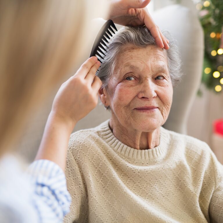 A health visitor combing hair of senior woman at home at Christmas time.