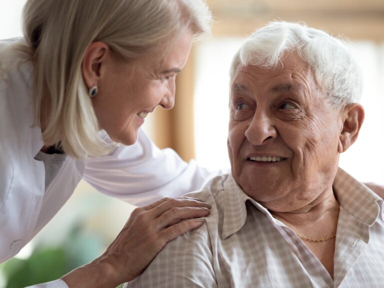 Close up middle-aged female doctor supporting older patient, touching shoulders, giving psychological help, caring mature female wearing white uniform talking with elderly man, healthcare concept