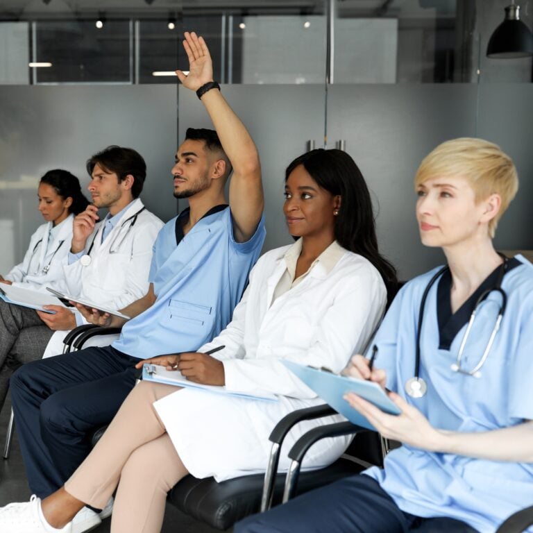 Arabic man doctor raising hand up while listening to speaker, multiethnic group of doctors attending medical conference or training at clinic. Education and Training for Health Care Professionals