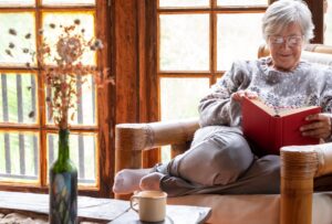 Attractive relaxed senior woman sitting at home in an armchair reading a book. Elderly smiling caucasian woman enjoying reading pleasure in retirement