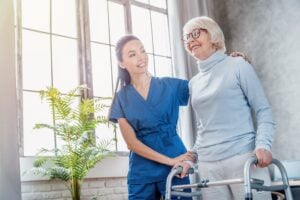Female asian nurse helping senior woman to walk with walker at home. Rehabilitation after injuries, traumas, walking disability and movement impairment. Senior life concept